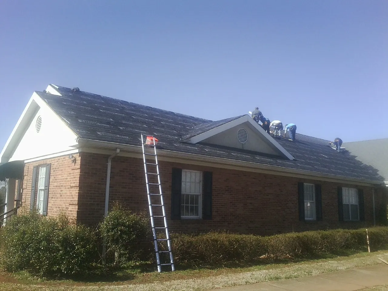 Crew tearing shingles off a brick ranch roof with a ladder set — Metal Roof Repair work by our crew in Knightsen