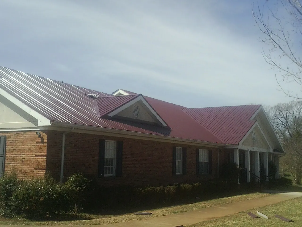 Red metal roof with gabled entries on a long brick building, from a Hail Damage Roof Repair job in Knightsen