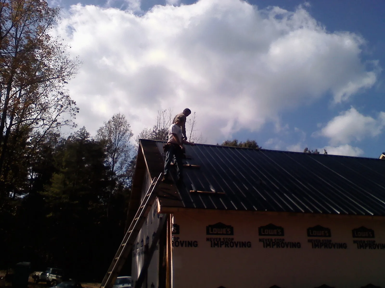 Roofer fastening dark metal panels high against a cloudy sky, from a Roof Inspection job in Knightsen