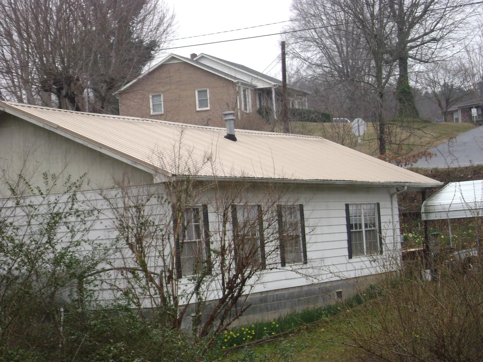 Tan metal roof on a white sided house set into a hillside — Commercial Roofing by Roofing Brothers in Knightsen